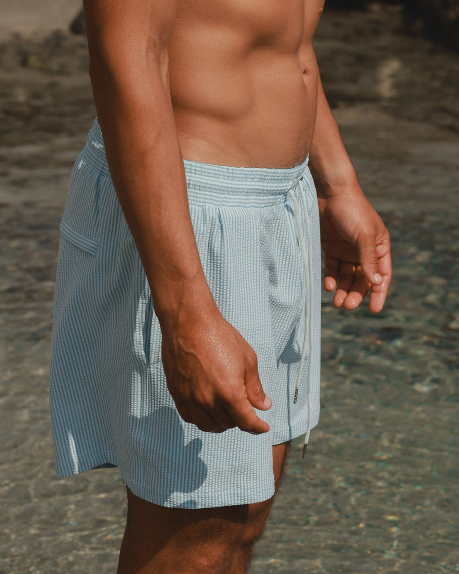 Person wearing light blue swim shorts with a subtle pattern on a beach.