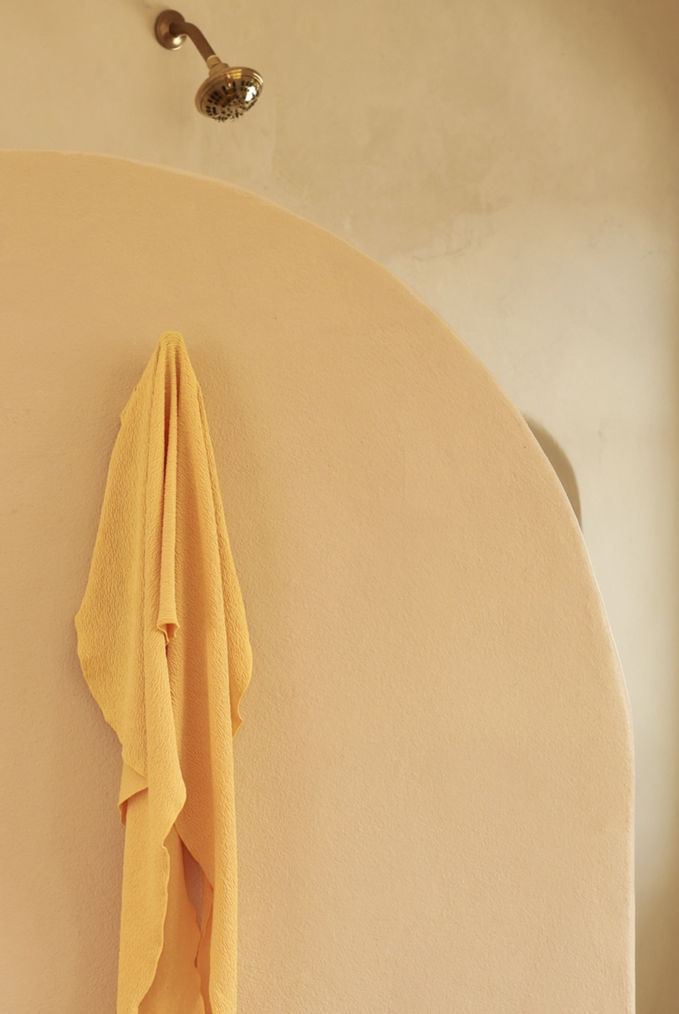 Yellow crinkle pareo hanging on a towel hook in a beige concrete shower