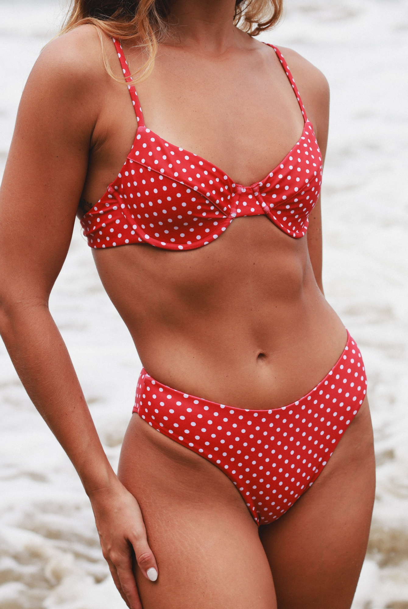 Close-up of a red polka dot bikini worn by a woman on a beach.