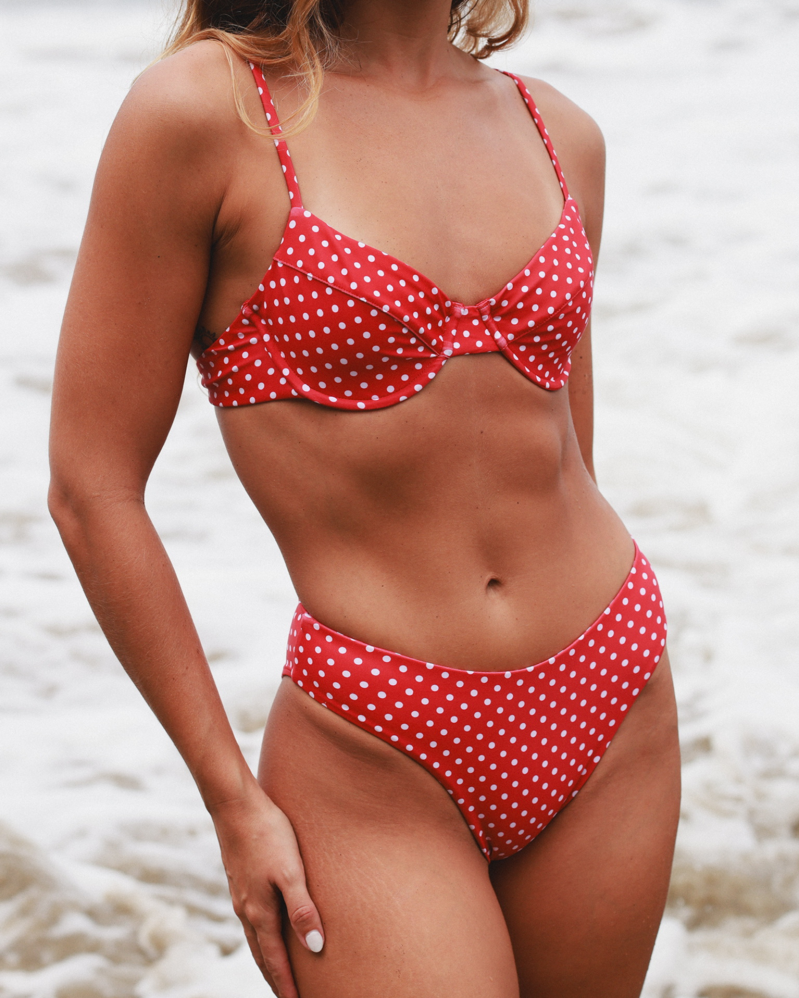 Close-up of a red polka dot bikini worn by a woman on a beach.