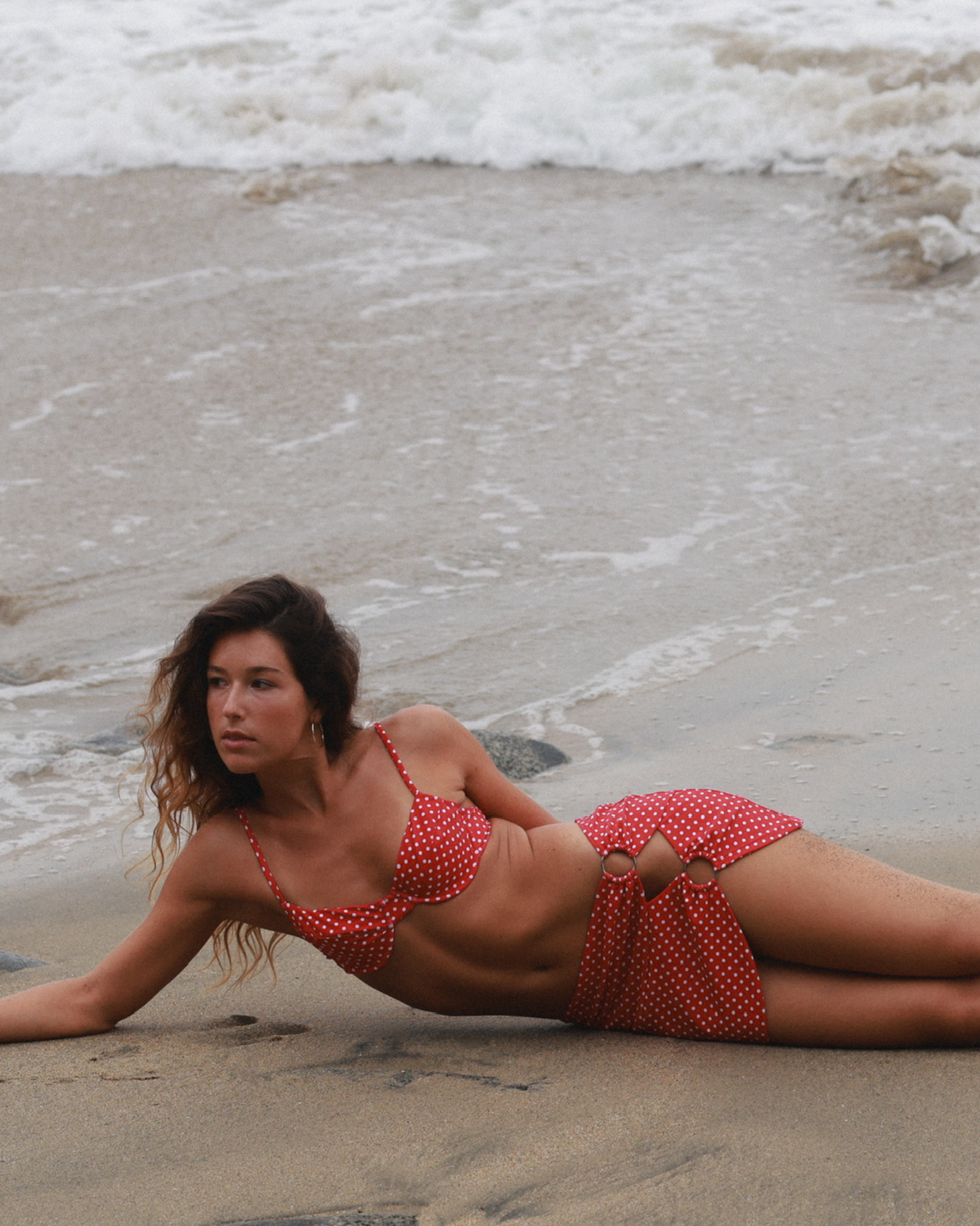 Woman in a red polka dot bikini lying on the beach with waves in the background