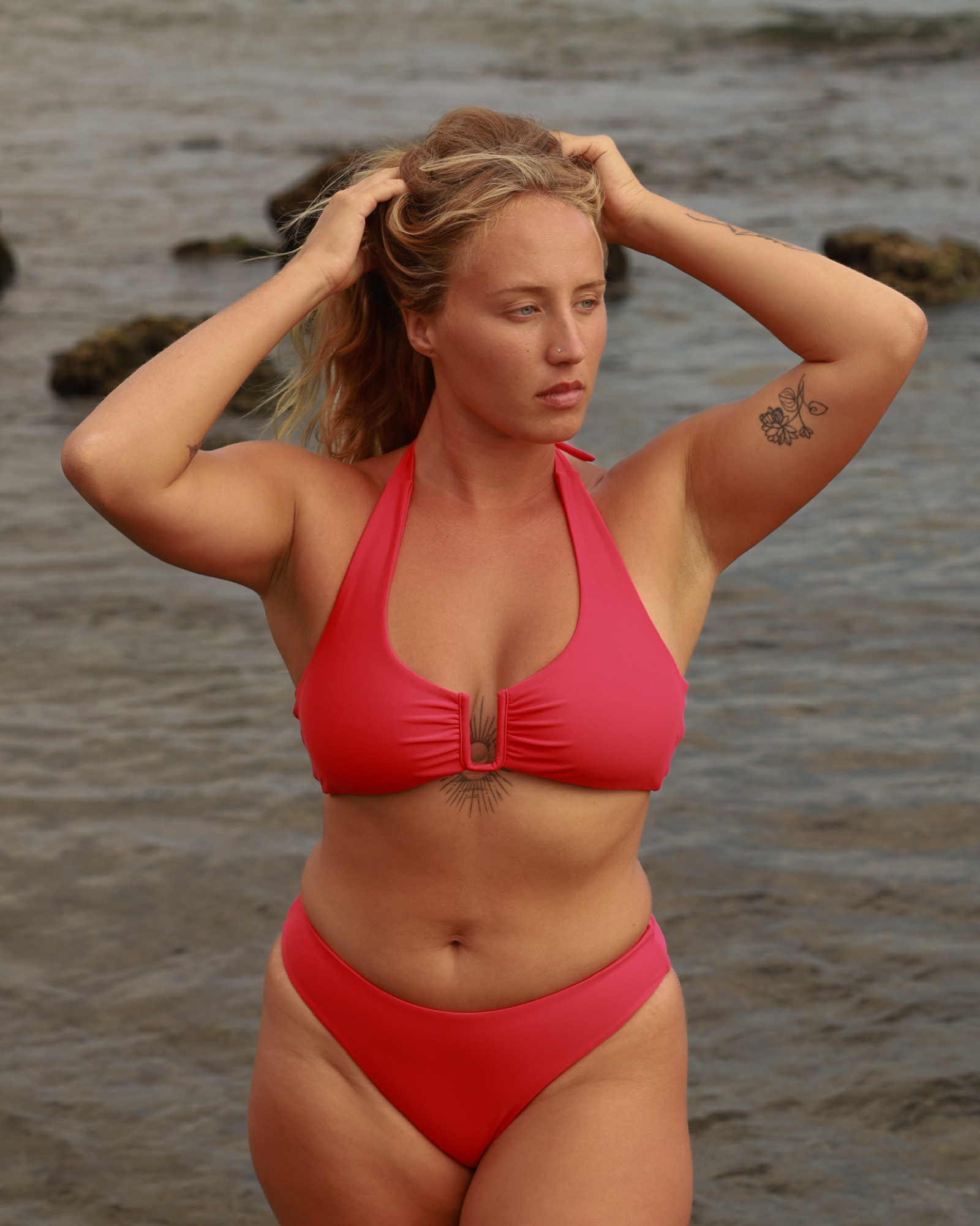 Woman wearing a red bikini standing on a beach by the water.