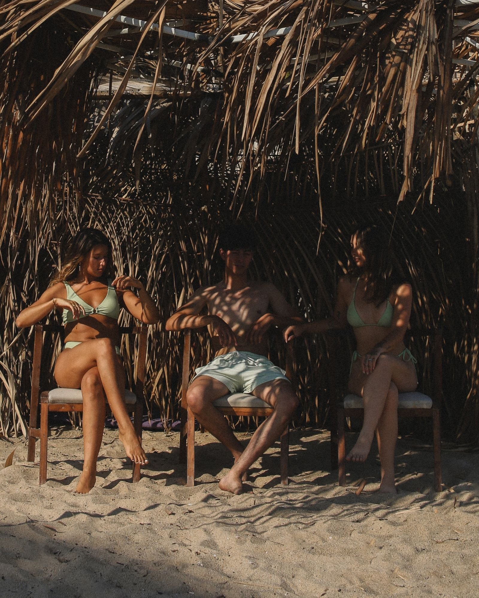 Des amis assis sur la plage portant des maillots de bain lime parfaitement assortis, en train de discuter.