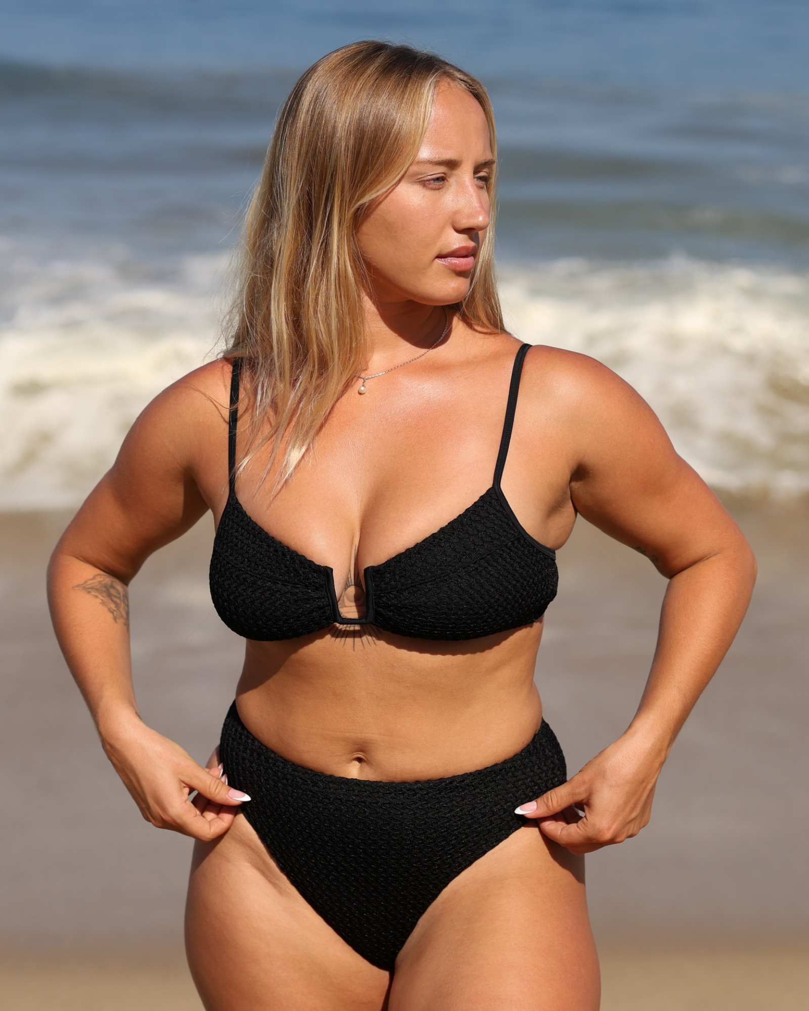 Woman wearing a black knitted bikini set with the beach in the backgroung