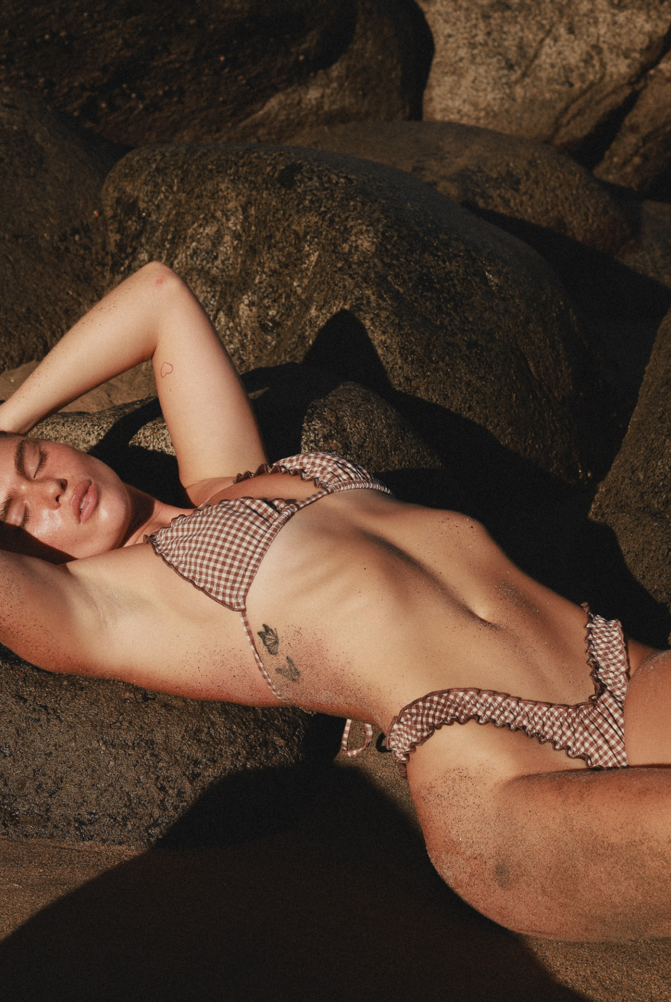 Relaxing on the rocks, a woman wears a stylish brown checkered bikini.