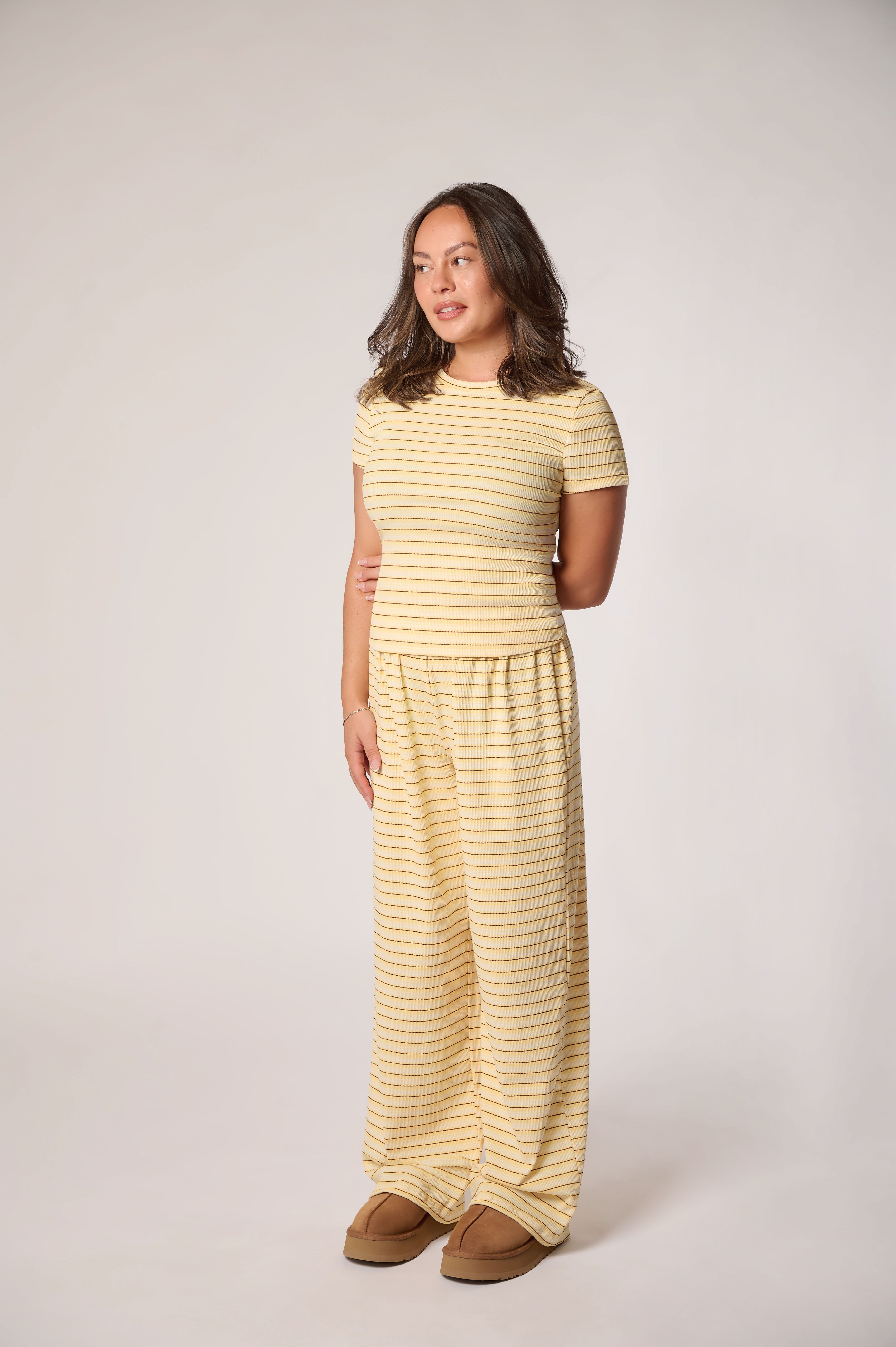 A woman modeling a matching two-piece loungewear set consisting of a short-sleeve top and wide-leg pants, both in a pale striped yellow.
