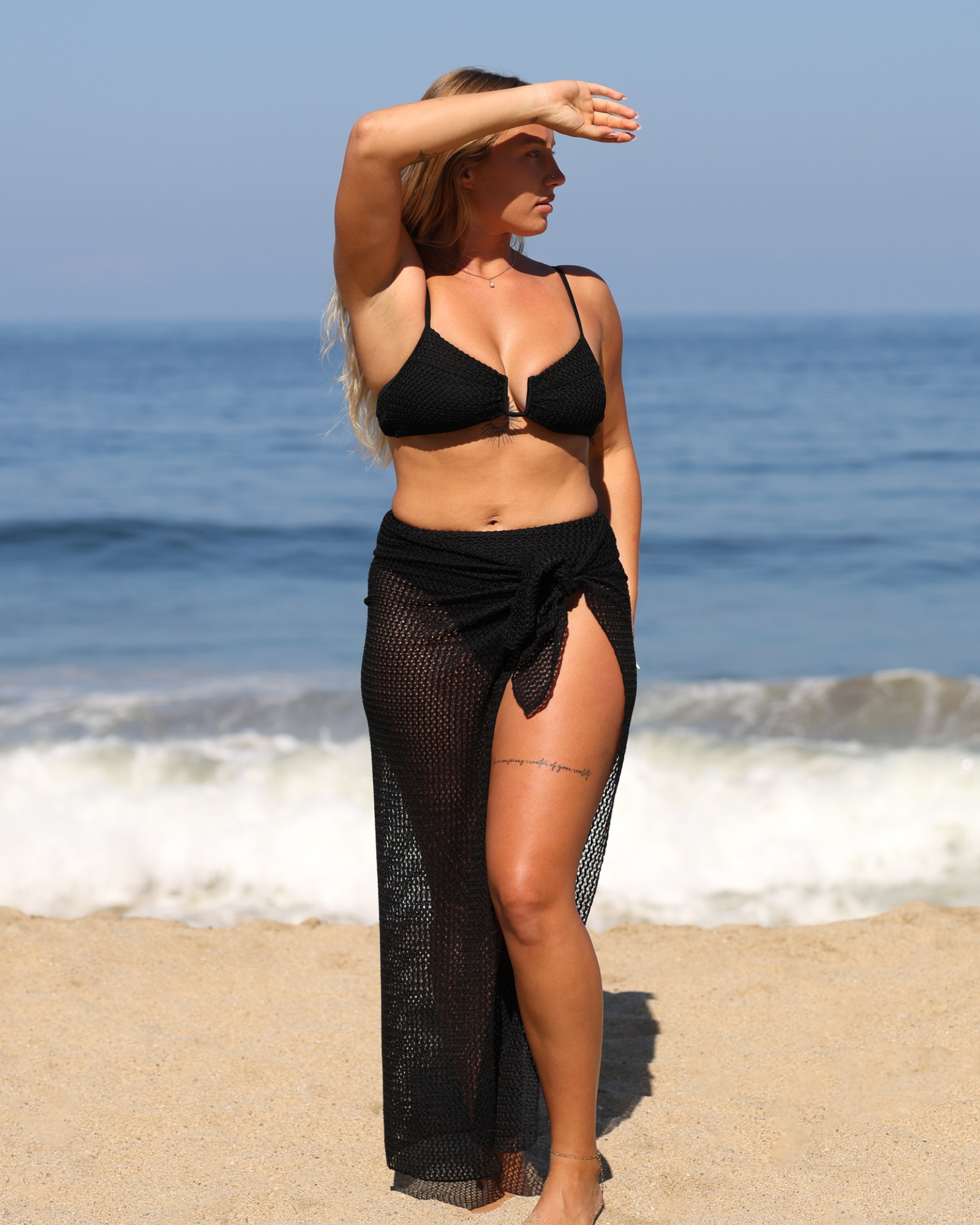 Tanned woman wearing a black bikini set with a mesh cover ups showing one leg