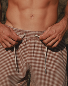 Close-up detail of a model wearing brown checkered swim shorts.