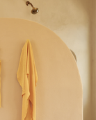 Paréo jaune crêpé suspendu à un crochet de serviette sur une douche en béton beige