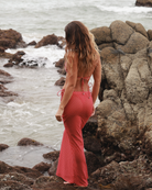 Woman back profile in a red polka dot skirt standing on rocky beach