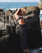 Woman in black polka dot bikini top and midi skirt set standing barefoot against a rock
