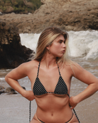 Woman in a black polka dot bikini standing on a beach with waves in the background