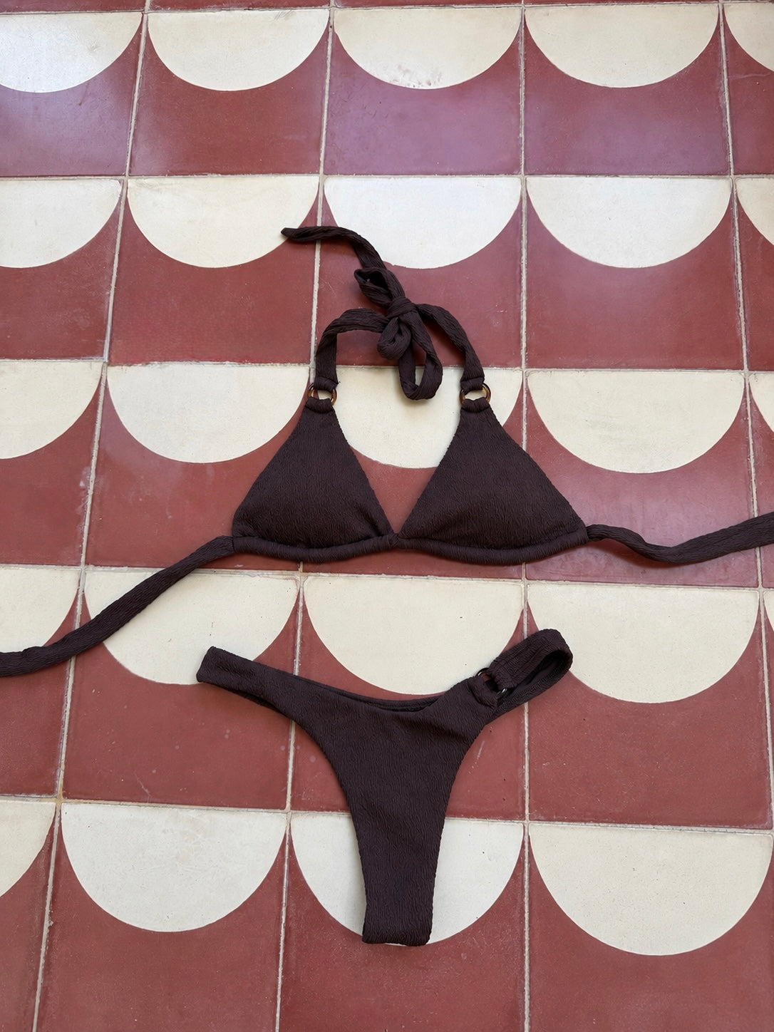 A dark brown montreal bikini set laid flat on a red and cream scalloped tile floor.