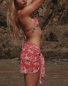 Woman in a reversible floral bikini and sarong standing on a beach with rocks in the background