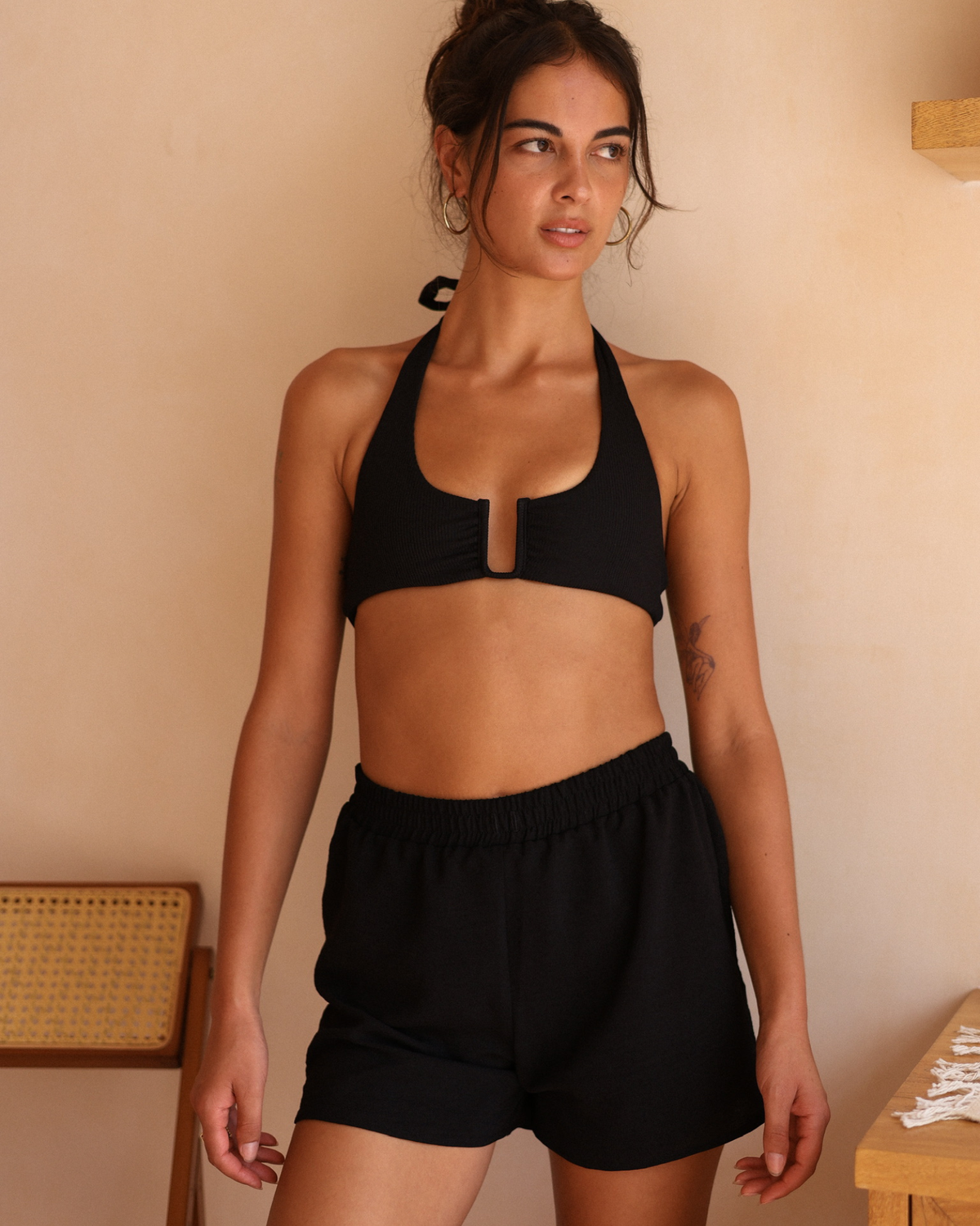 A close-up of a woman wearing a black bikini top and matching shorts, styled with a black wrap top tied at the waist.