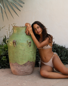 Woman wearing a low-rise polka dot bikini bottom, sitting next to a large green ceramic jar outdoors