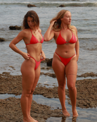 Two women in red bikinis standing on a beach.