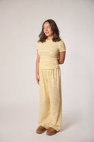 A woman modeling a matching two-piece loungewear set consisting of a short-sleeve top and wide-leg pants, both in a pale striped yellow.