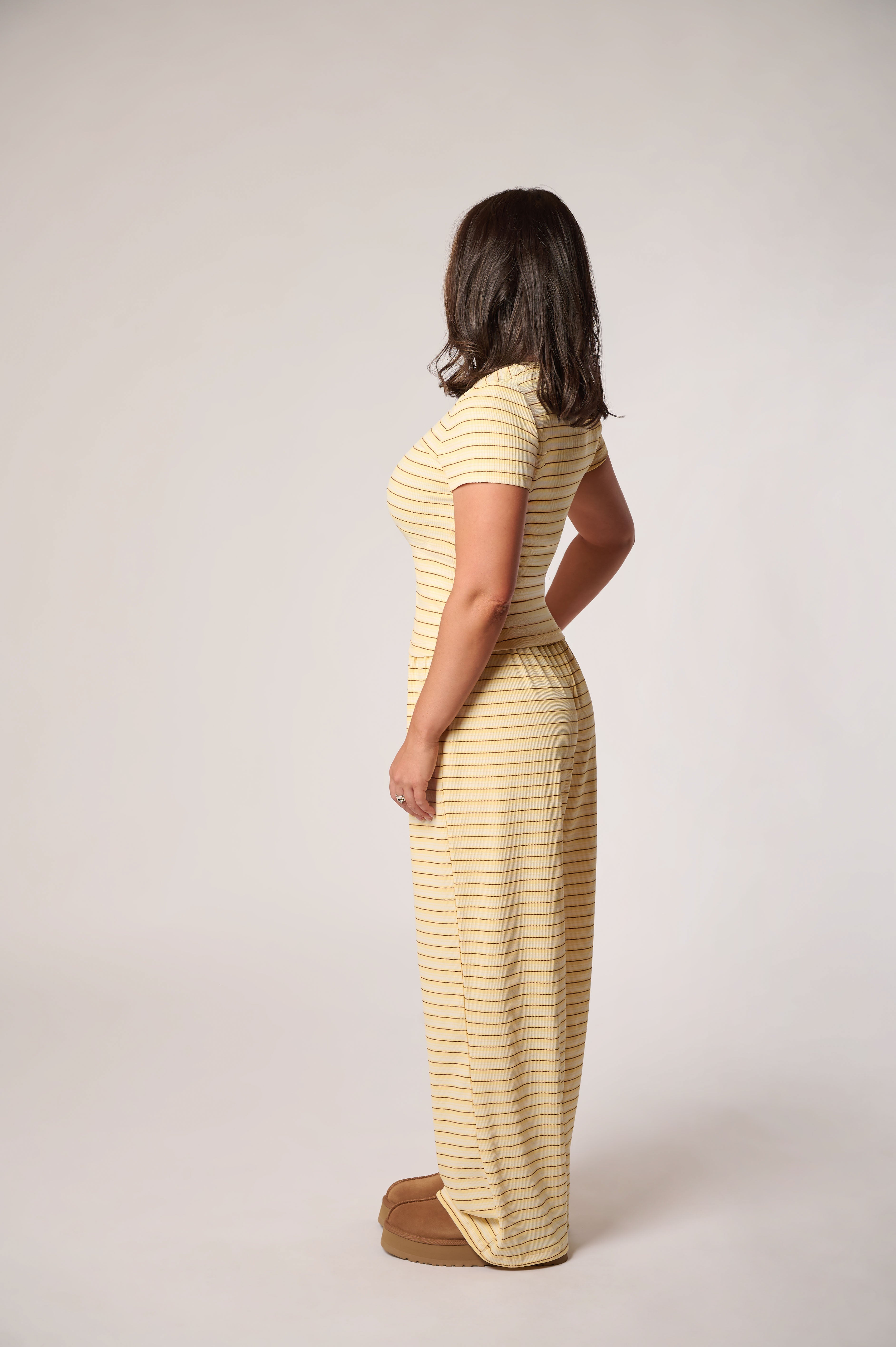 A woman stands in profile wearing a matching striped yellow kit photographed against a plain light gray studio background.