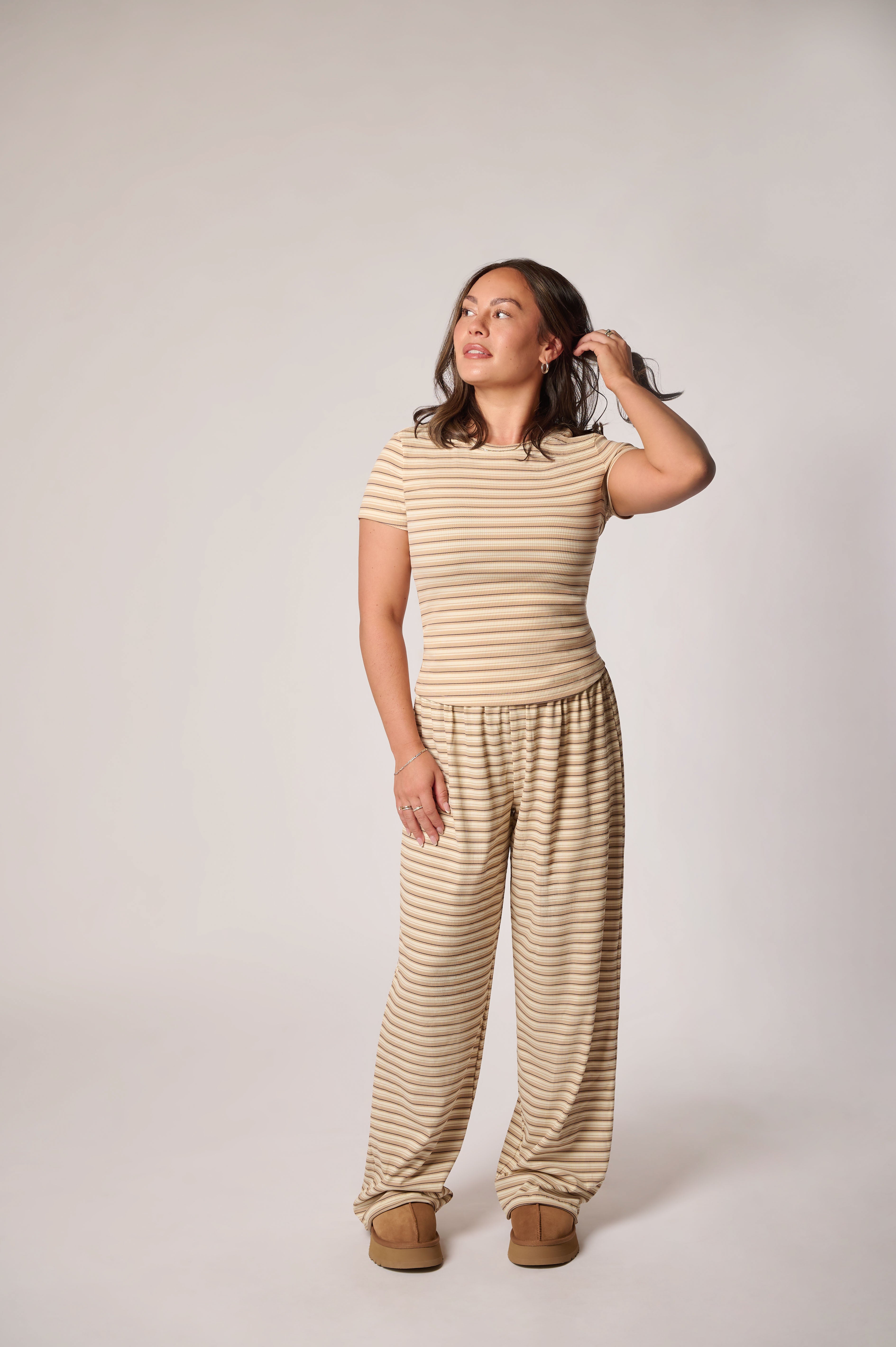 A woman modeling a matching beige and cream striped loungewear set, against a plain light gray studio background.