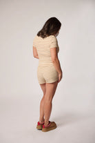 A woman stands with her back to the camera wearing a beige and white horizontally striped two pieces, wearing brown platform shoes.