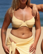 Woman standing on a beach wearing a yellow rib underwired bikini top