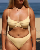 Tanned woman wearing a butter yellow ribbed bikini set with a beach background
